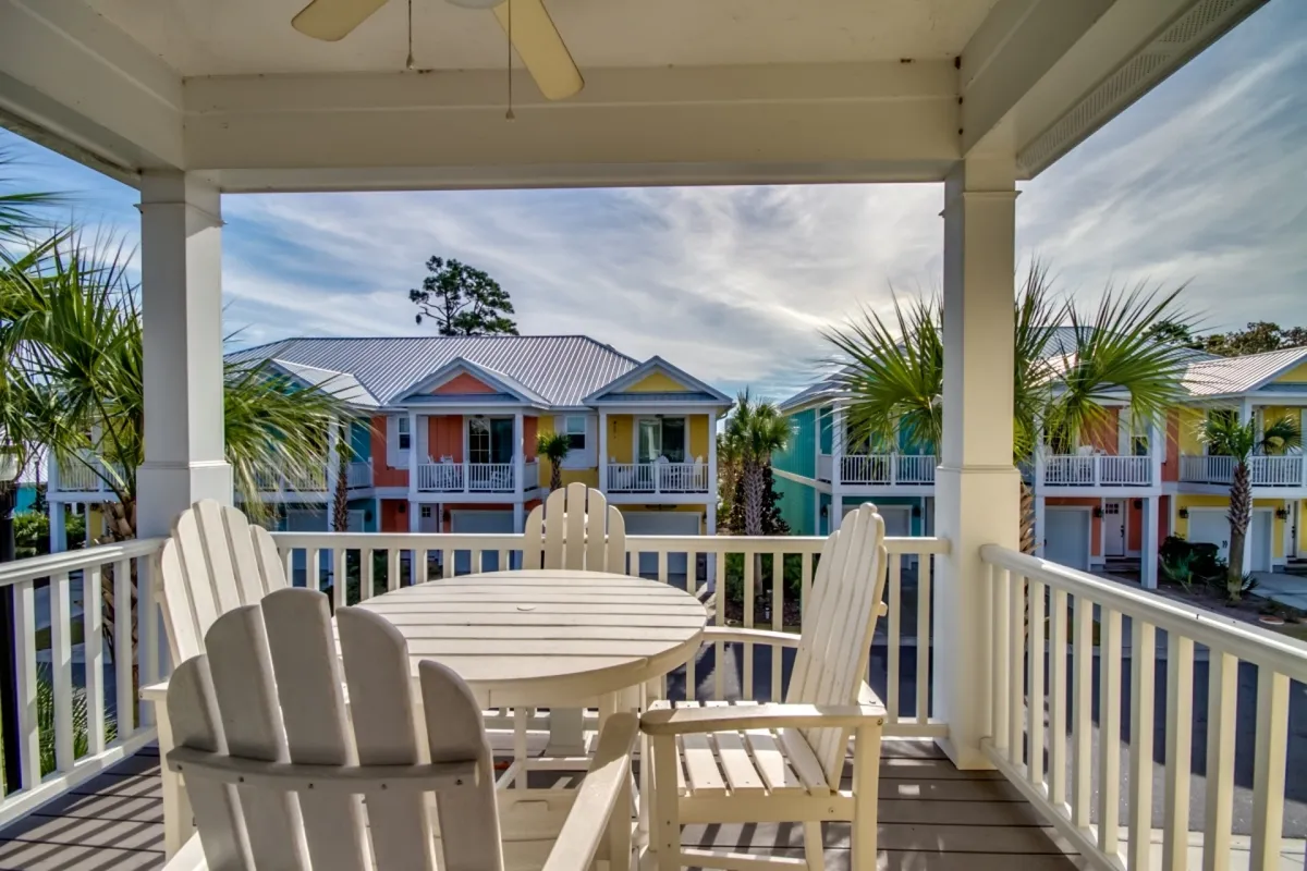 A cheerful outdoor seating area on a covered second-floor balcony, featuring comfortable chairs and a small table. The view includes colorful resort buildings and swaying palm trees, evoking a relaxed, tropical vibe. The setting is ideal for morning coffee or relaxing evenings while enjoying fresh air and privacy.