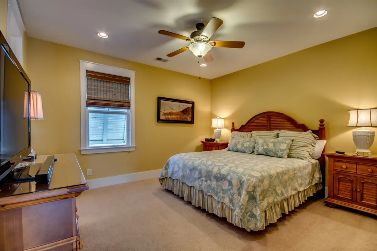 This image captures a serene master bedroom featuring a king-sized bed adorned with a plush, floral bedspread. Wooden nightstands and a TV complete the scene, with natural light softly illuminating the room, creating a tranquil atmosphere ideal for restful nights.