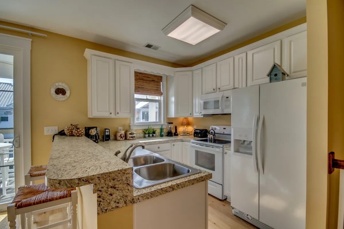 A welcoming kitchen with granite countertops, white cabinetry, and modern appliances including a dishwasher, blender, and coffee maker. A window fills the space with natural light, and the open layout allows for easy interaction with the dining and living areas nearby.