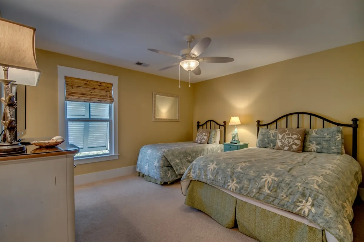 This photo showcases the second bedroom, which offers flexible sleeping arrangements with both a queen and a twin bed. Patterned bedding, a table lamp, a decorative mirror, and a window with blinds contribute to a cozy, well-lit space suitable for families or friends.